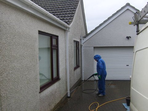 man cleaning a pebbledash wall ready for painting